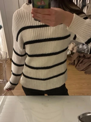 Vit stickad tröja med svarta ränder - Säljer en vit stickad tröja med svarta horisontella ränder. Tröjan har en rak passform, ribbstickade muddar och rund halsringning. Perfekt för en chill och stilren look. Materialet känns mjukt och mysigt. Tröjan finns även på min vinted - selmaoverfjord 