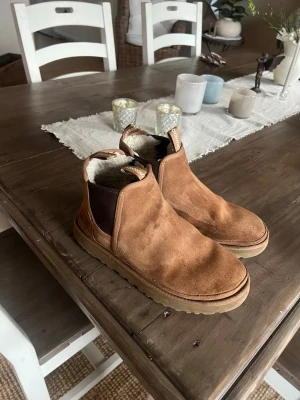 Bruna Chelsea boots från UGG - Säljer ett par bruna Chelsea boots från UGG i mocka med elastiska partier på sidorna och mjukt, vitt foder inuti. Yttersulan är i gummi och bootsen har en klassisk, stilren form som passar till många olika outfits.