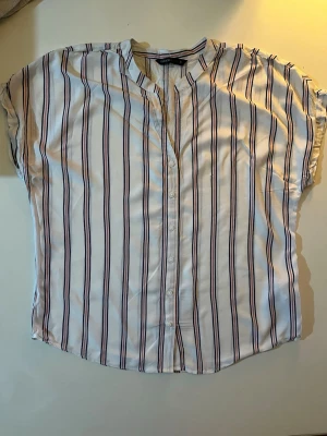 Randig skjorta från DeFacto - Kortärmad skjorta från DeFacto i vitt med blå och rosa ränder. Skjortan har knappar framtill och en avslappnad passform. Perfekt för en chill och stilren look. Aldrig använd, helt ny men saknar prislapp.