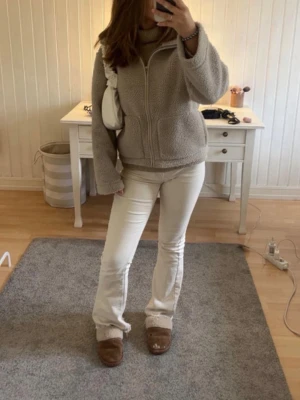 Beige teddyjacka med dragkedja - Mysig beige teddyjacka med hög krage och dragkedja framtill. Jackan har två fickor och en avslappnad passform som ger en trendig look. Perfekt för lager-på-lager och passar till många olika outfits. Materialet är fluffigt och ger en soft vibe.