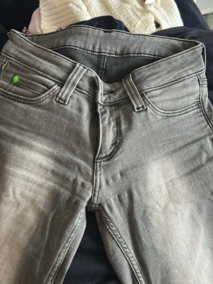 Grå raka jeans med slitningar - Snygga grå jeans med raka ben och diskreta slitningar framtill. Klassisk femficksmodell med en liten grön detalj på myntfickan. Jeansen har normal midja och är tillverkade i stretchigt denimtyg för extra komfort.