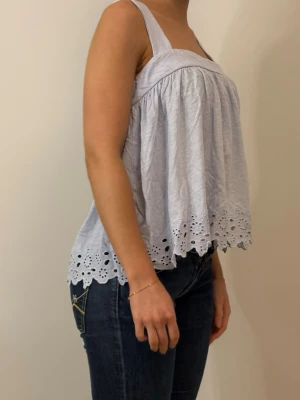 Ljusblå ärmlös linnetopp med broderi - Söt ljusblå linnetopp med breda axelband och broderade blommor längs fållen. Toppen är luftig och har en lös passform, perfekt för varma dagar. Materialet känns mjukt och toppen har en romantisk känsla med sina detaljer.