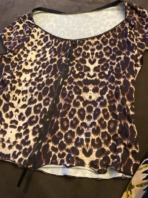 Leopardmönstrad topp med snörning - Cool topp i leopardmönster med snörningsdetalj framtill. Tillverkad i mjuk polyesterblandning med stretch för skön passform. Kortärmad och rundad halsringning med dekorativ kant. Perfekt för dig som vill sticka ut lite extra.