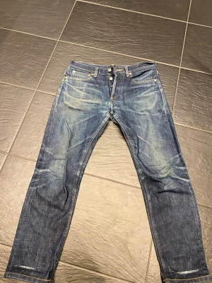 APC selvedge  - Säljer ett par klassiska blå jeans med raka ben och knappgylf. Jeansen har snygga slitningar och kontrastsömmar, samt fem fickor. Perfekta för en avslappnad och trendig look. Materialet är kraftig denim i bomull. Längd: 89 cm, Midja : 40 cm. Skriv för mer info.