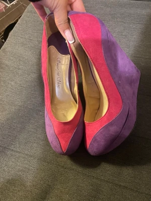 Färgglada pumps från Sugarfree Shoes - Säljer ett par unika pumps från Sugarfree Shoes i mockaimitation. Skorna har en cool färgkombination av lila och ceriserosa, med kilklack och rundad tå. Perfekta för dig som vill sticka ut med din stil!