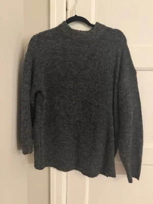 Mörkgrå stickad tröja - Mysig mörkgrå stickad tröja med lång ärm och rak passform. Tröjan har en enkel design utan synliga detaljer eller mönster och är tillverkad i ett fluffigt, mjukt material som känns skönt mot huden. Perfekt för kyliga dagar. Xs från lager 157 men i väldigt fint material för att vara lager 157