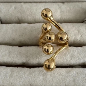 Guldfärgad statementring med klot - Unik guldfärgad ring med flera glänsande klot i olika storlekar som ger en modern och iögonfallande look. Ringen har en öppen design och passar perfekt för dig som vill sticka ut med dina accessoarer.