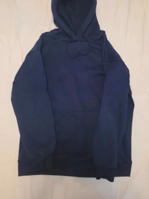 Mörkblå hoodie med huva - En enkel och stilren mörkblå hoodie med huva och dragsko. Hoodien har långa ärmar, ribbade muddar och en klassisk passform. Perfekt för en avslappnad look och funkar året runt. Materialet känns mjukt och bekvämt mot huden.