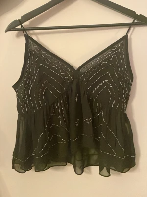 Svart linne med silver detaljer - Säljer ett svart v-ringat linne med silver detaljer. Säljer då den inte passar mig!