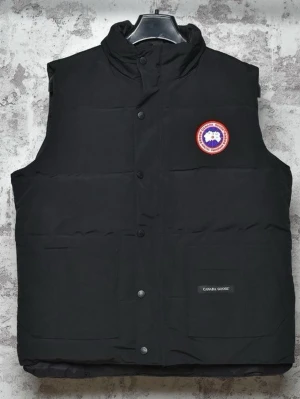 Svart dunväst från Canada Goose - Snygg svart dunväst från Canada Goose med klassisk logotyp på bröstet och diskret varumärkeslapp vid fickan. Västen har hög krage, tryckknappar och är vadderad för extra värme. Perfekt för lager-på-lager och streetwear-stil.