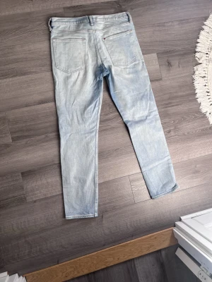 Ljusblå raka jeans - Säljer ett par ljusblå jeans med rak passform och klassisk femficksdesign. Jeansen har bälteshällor och knappgylf. Perfekta för en avslappnad och trendig look.
