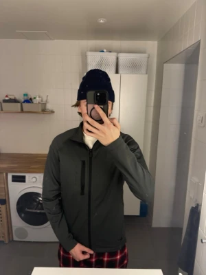 Svart ziptröja från Sail Racing - Snygg svart ziptröja från Sail Racing med dragkedja framtill och bröstficka med dragkedja. Tröjan har en stilren design och logga på bröstet. Perfekt för dig som gillar sportig och enkel stil.