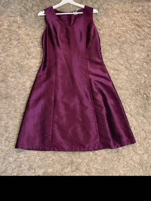 Vinröd kostymklänning med kavaj - Säljer en vinröd kostymklänning i glansigt tyg med matchande kavaj. Klänningen är ärmlös med v-ringning och kavajen har trekvartsärm och snygga rynkdetaljer framtill. Perfekt för dig som vill sticka ut med en elegant look.