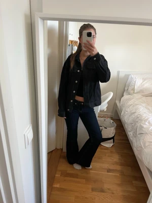 Svart jeansjacka med silvriga knappar - Snygg svart jeansjacka med klassisk passform och silvriga knappar framtill. Jackan har två bröstfickor med lock och knäppning samt raka ärmar. Perfekt att slänga över en topp för en cool look.