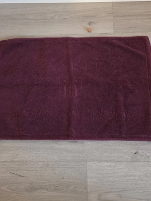 Mörklila badrumsmatta från Gant - Säljer en badrumsmatta från Gant. Mattan är rektangulär och tillverkad i mjuk frotté, 