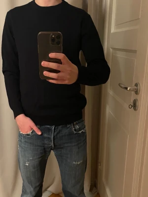 Marinblå stickad tröja i merinoull  - En stilren marinblå stickad tröja i merionull med rund halsringning och långa ärmar. Tröjan har en klassisk passform och ribbstickade muddar vid ärmslut och nederkant. Perfekt för en enkel och clean look. 