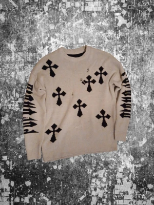 Beige stickad tröja med svarta kors - Stickad beige tröja med svarta korsmönster framtill och baktill samt grafiska svarta detaljer längs ärmarna. Tröjan har rund halsringning och är size s kommer med hål på den men det är själva designen kom med bud 