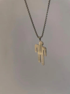 Billie Eilish halsband - Snyggt halsband i silverfärg med en unik, stilren berlock formad som en stiliserad människa. Kedjan är tunn och har klassisk länkdesign. Perfekt accessoar för dig som gillar minimalistiska smycken med en twist. Materialet ser ut att vara metall.