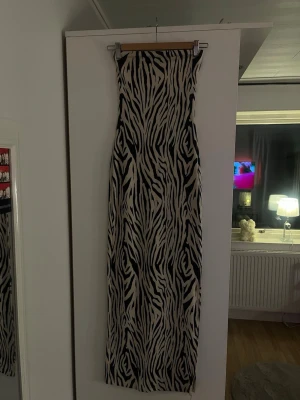 Zebramönstrad långklänning - Säljer en lång tubklänning med zebramönster från bershka. Klänningen har en rak passform och en slits på vänster ben. Den är ankellång och slutar vid vristen. Den är bara använd några gånger och i jätte bra skick. 