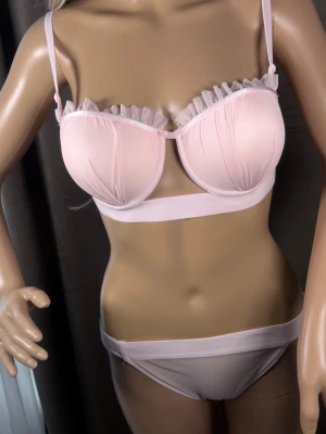 Ljusrosa underklädesset med volang - Sött ljusrosa underklädesset med bygel-bh och matchande trosa. Bh:n har tunna axelband och dekorativa volanger längs kuporna. Materialet är tunt och mjukt, troligen mesh eller polyester. Perfekt för dig som gillar romantiska detaljer.