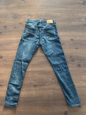 Blå slim fit jeans med slitningar - 32/32 Snygga blå slim fit jeans med lätt slitna detaljer och klassisk femficksdesign. Jeansen har en läderpatch bak i midjan och smal passform hela vägen ner. Perfekta för en avslappnad och trendig look.