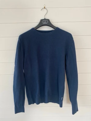 Mörkblå stickad tröja - En stilren mörkblå stickad tröja med rund halsringning och långa ärmar. Tröjan har ribbstickade muddar vid ärmslut och nederkant. Perfekt för lager-på-lager och enkel att matcha med olika outfits.