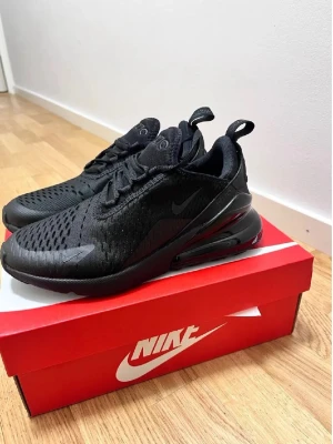 Nike Air Max 270 helsvarta sneakers - Nike Air Max 270 sneakers i helsvart med mesh-ovandel och synlig Air Max-dämpning i hälen. Snygg sportig design med diskret Nike-logga på sidan och dragflik bak. Perfekta för dig som gillar en clean och modern look.