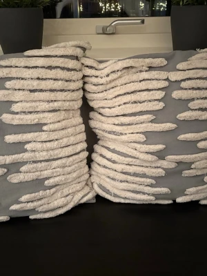 Två kuddfodral River från Classic Collection i nyskick  - Två kuddfodral från Classic Collection i grått och vitt. Modellen heter River. Mått 50x50. Fint mönster med upphöjd lugg. Kuddarna är i nyskick, sparsamt använda. Nypris gör båda ca 1100 kr.