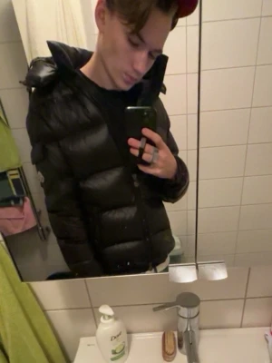 Moncler Maya  - Snygg svart dunjacka från Moncler med glansig finish och klassisk Moncler-logga på ärmen. Storlek 2 vilket motsvarar S/M passar dig som är 170-185. Finns en skavank som är lagat med en laglapp det är ett litet hål vid bröstet som inte läggs till märke och går enkelt att sy ihop