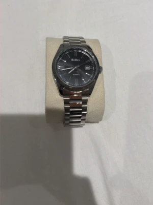 Silverfärgad klocka  - Stilren klocka  med silverfärgad länkarmband och svart urtavla. Klockan har datumvisning och klassisk rund form. Perfekt accessoar för dig som gillar en clean och tidlös look.