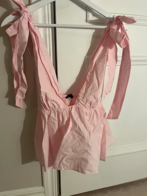 Ljusrosa kort klänning med knyt - Supersöt ljusrosa kort klänning från zara med djup v-ringning och knyt på axlarna. Klänningen har en luftig passform och är tillverkad i bomull, perfekt för varma dagar.