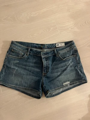 Blå jeansshorts med slitningar - Snygga blå jeansshorts  i klassisk femficksmodell. Shortsen har slitna detaljer framtill och normal passform. Perfekta för varma dagar och enkla att matcha med olika toppar.