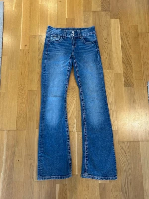 Blå lågmidjade bootcut jeans med dubbla knappar  - Snygga blå bootcut jeans med dubbla knappar i midjan från Gina tricot. Jeansen har en lätt tvättad look och kontrastsömmar. Perfekta för dig som gillar en avslappnad men trendig stil. Storlek 158