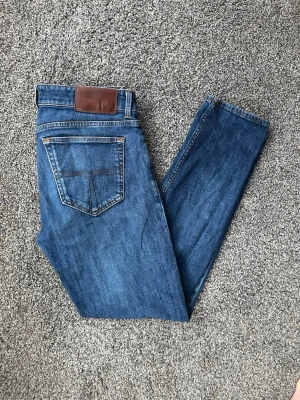 Blå slim fit jeans från tiger of sweden - Snygga blå slim fit jeans med klassisk femficksdesign och läderpatch bak i midjan. Jeansen har en rak passform och är tillverkade i ett mjukt denimtyg med lätt stretch för extra komfort.