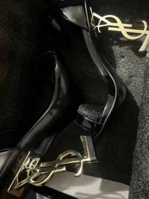 Ysl heels - Säljer ett par svarta lackpumps från Saint Laurent med ikonisk YSL-logga i guld som klack. Skorna har öppen tå och elegant, modern design. Perfekta för dig som vill sticka ut med exklusiva detaljer och lyxig känsla. Köpte för 13000kr