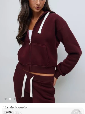 Ziphoodie - Mysig vinröd hoodie med dragkedja och huva från Gina. Har vita snören i huvan och en stor magficka framtill. Tillverkad i mjukt sweatshirtmaterial, perfekt för en avslappnad stil.