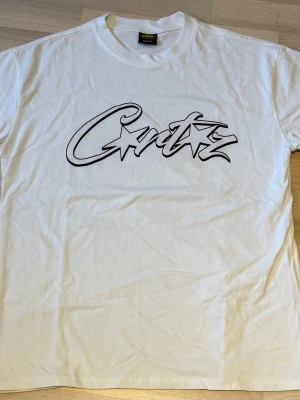 Vit t-shirt från Corteiz med tryck fram - Vit t-shirt från Corteiz med ett stort svart grafiskt tryck på bröstet. Klassisk rund halsringning och korta ärmar. Perfekt för en avslappnad streetwear-look. Den är true to size, alltså passar M bra, jag har själv S och tycker den är lite för stor för mig - ALDRIG ANVÄND!