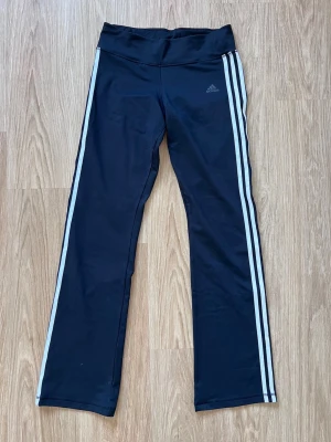 Svarta utsvängda träningsbyxor från Adidas, storlek M - Svarta träningsbyxor från Adidas med utsvängda ben och mid waist. Väldigt stretchiga och passar till träning eller vardag! 93% polyester och 7% spandex. Mycket bra skick. 