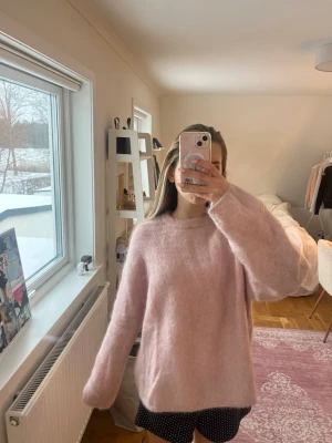 Ljusrosa fluffig mohair stickad tröja - Mysig och oversized stickad tröja i ljusrosa färg med rund halsringning och långa ärmar. Tröjan har en fluffig och mjuk känsla, perfekt för kalla dagar. Passar till både jeans och kjol för en avslappnad look.