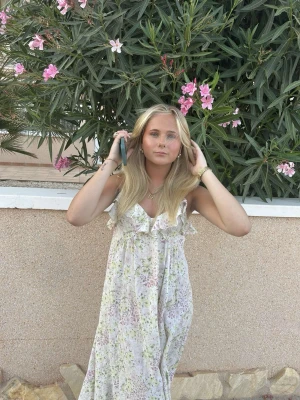 Blommig långklänning med volang från H&M - Söt långklänning i vitt med blommigt mönster i pastellfärger. Klänningen har volangdetaljer vid bysten och är ärmlös med v-ringning. Perfekt för varma dagar och somriga tillfällen.