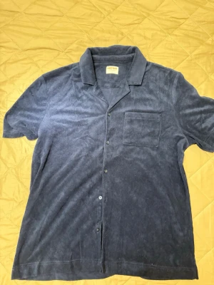 Mörkblå frottéskjorta - Kortärmad skjorta i mjuk mörkblå frotté. Klassisk krage, knappstängning framtill och en bröstficka. Perfekt för en avslappnad och cool stil.