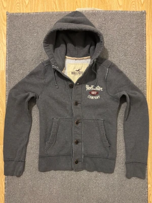 Vintage Hollister Cardigan Med Knappar - Säljer denna otroliga sällsynta och feta Hollister cardigan med knappar | Väldigt bra skick förutom några fläckar, se bild!! Därav billigare pris | Längd ≈ 62cm, Bredd armhåla - armhåla ≈51 cm | Modell 175, 68 kg | PRIS KAN DISKUTERAS