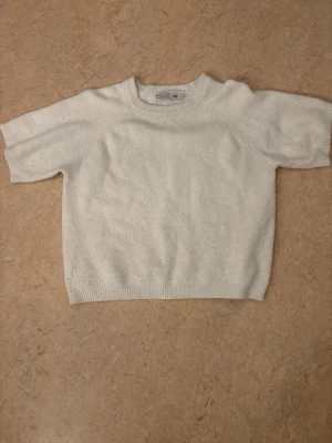 Vit stickad tröja från 157 - Säljer en enkel och stilren vit stickad tröja från 157. Tröjan har korta ärmar, rund halsringning och ribbade muddar vid ärmslut och nederkant. 