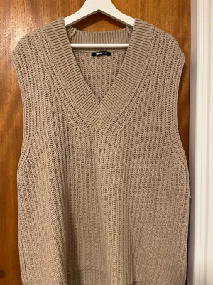 Beige stickad väst från Gina Tricot - Säljer en beige stickad väst från Gina Tricot i storlek M. Västen har djup v-ringning, bred ribbad kant och är ärmlös. Perfekt att styla över en skjorta eller t-shirt för en trendig lager-på-lager-look. Är väldigt bra skick