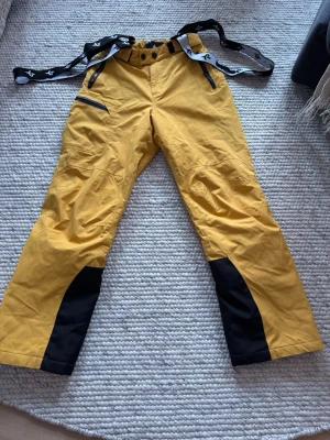 Gula skidbyxor Cross Sportswear XS - Säljer ett par gula täckbyxor från Cross Sportswear i storlek XS. Byxorna har svarta förstärkningar vid bensluten, svarta dragkedjor och justerbara hängslen. Perfekta för vinterns alla äventyr och riktigt snygga med sin kontrastdesign.
