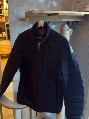 Svart Parajumpers pufferjacka M - Säljer en svart pufferjacka från Parajumpers i storlek M. Jackan har quiltad design, gul detalj vid halsen och klassisk PJS-patch på ärmen. Lättviktig och med dragkedja framtill. Perfekt för dig som vill ha en clean och funktionell look.