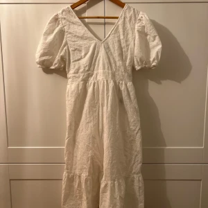 Vit klänning med puffärmar - Charmig vit klänning med puffiga kortärmar och v-ringning. Den har en söt knytning i ryggen och är dekorerad med diskreta broderier. Perfekt för sommarens fester eller en mysig vårdag. Klänningen har en luftig passform och är gjord i ett lätt material som känns skönt mot huden. Använt två tre gånger bara.