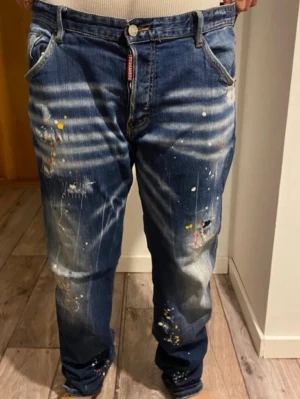 Dsquared2 paint splatter jeans - Säljer ett par blå jeans från Dsquared2 i baggy modell med coola färgstänk och slitningar. Jeansen har låg midja, raka ben och klassiska fem fickor. Materialet är jeans med tydliga tvättade detaljer och patch bak. 
