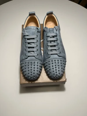 Smoke grey mocka sneakers från Louboutin - Säljer ett par grå sneakers från Christian Louboutin i mocka med ikoniska röda sulor och coola nitar över tån. Box och allt annat ingår!
