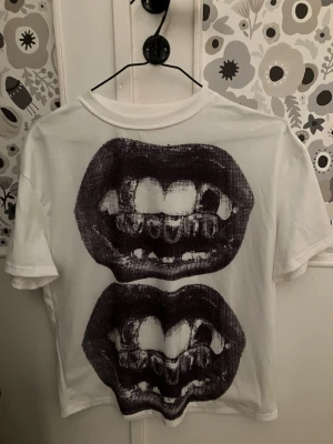T-shirt med munnar på - Jättecool t-shirt med gråa munnar på. Munnarna visar tänderna, vissa tänder är silvriga och har mönster på. Den är lite oversize! Använd bara några få gånger!